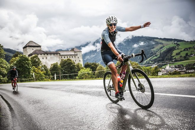 Juliet waving to the camera while cycling past a castle on a wet alpine road