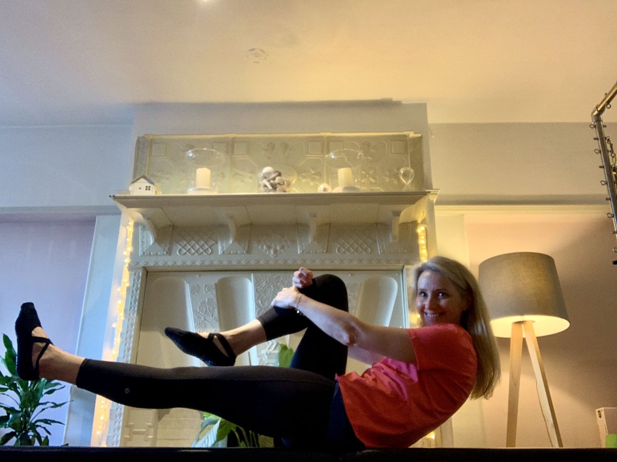 Juliet balancing in a seated pose on apparatus in her home Pilates studio