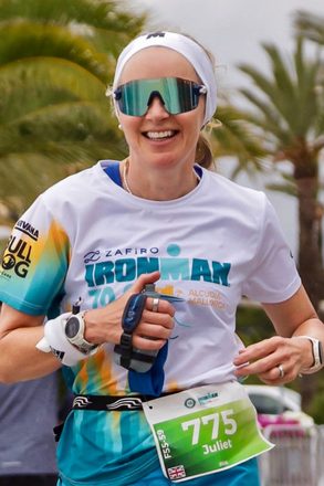 Juliet smiling broadly mid-run at Ironman 70.3 Alcudia Mallorca, wearing race number 775