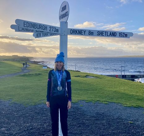 Juliet wearing a medal at the John o' Groats signpost at sunset