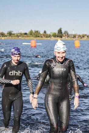 Juliet smiling as she wades out of an open-water swim in a wetsuit